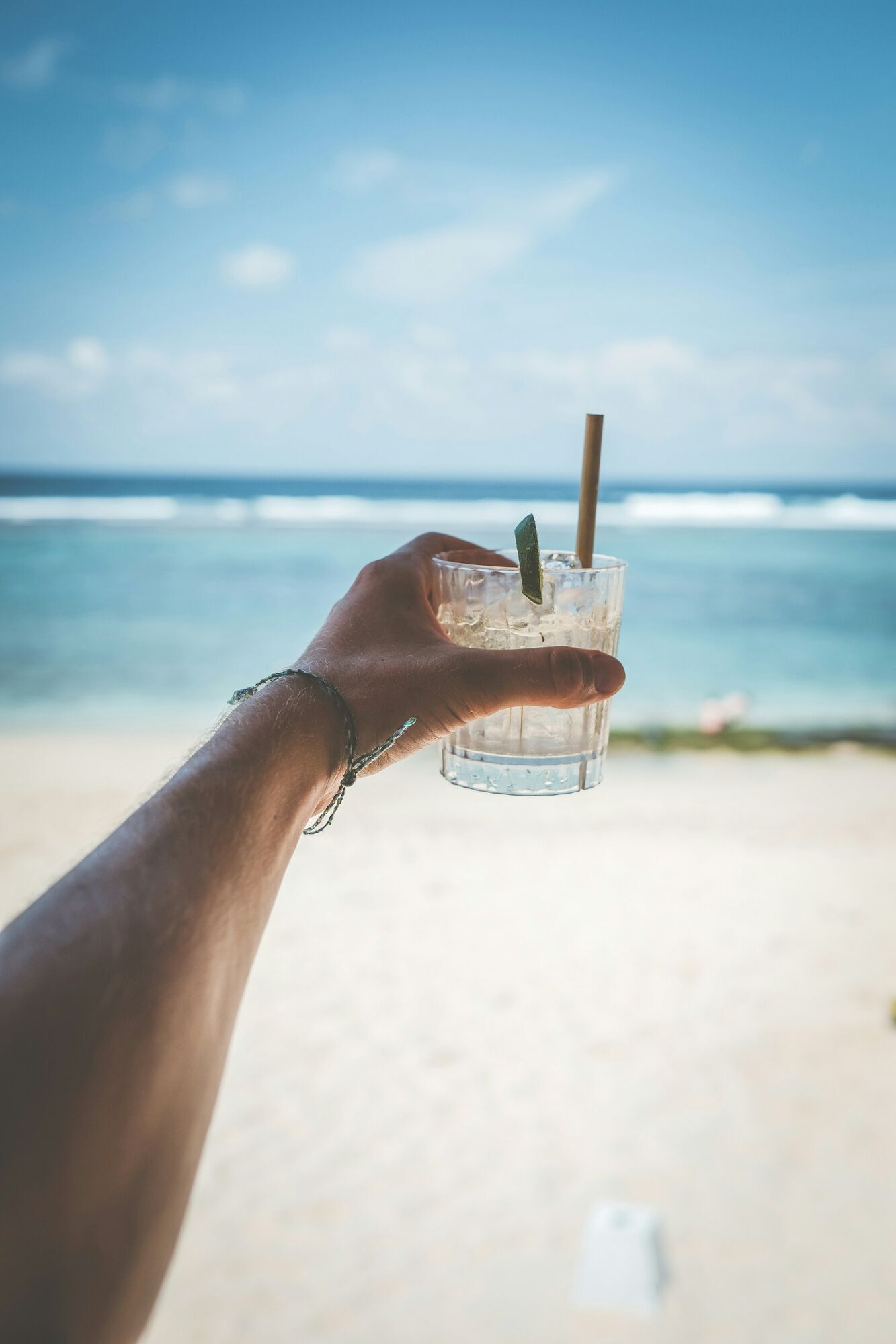 Hand holding a drink by the beach