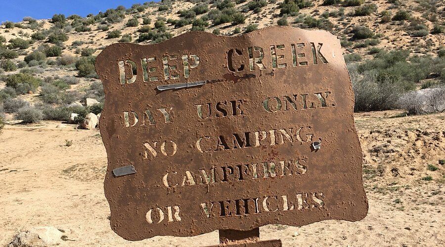 Rustic sign at Deep Creek Hot Springs with usage rules in a desert setting