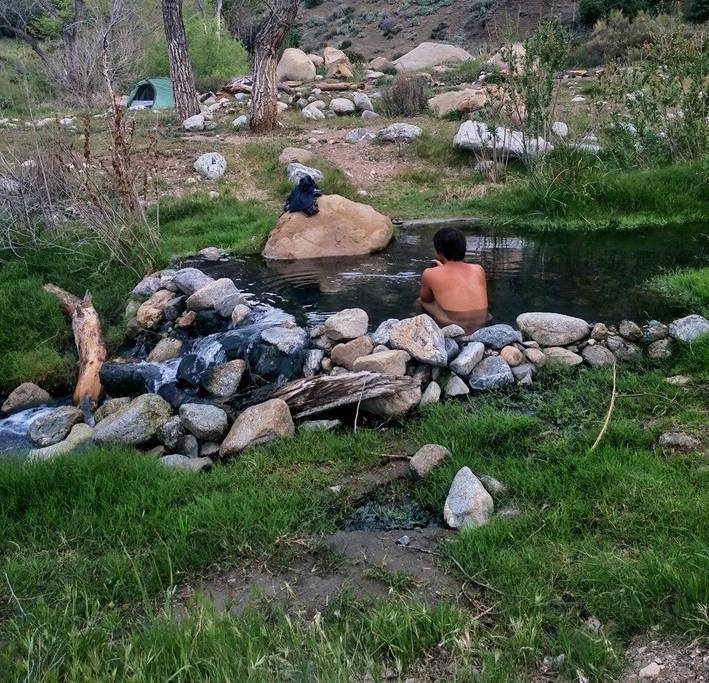 A person relaxing in a natural hot spring surrounded by greenery and rocks