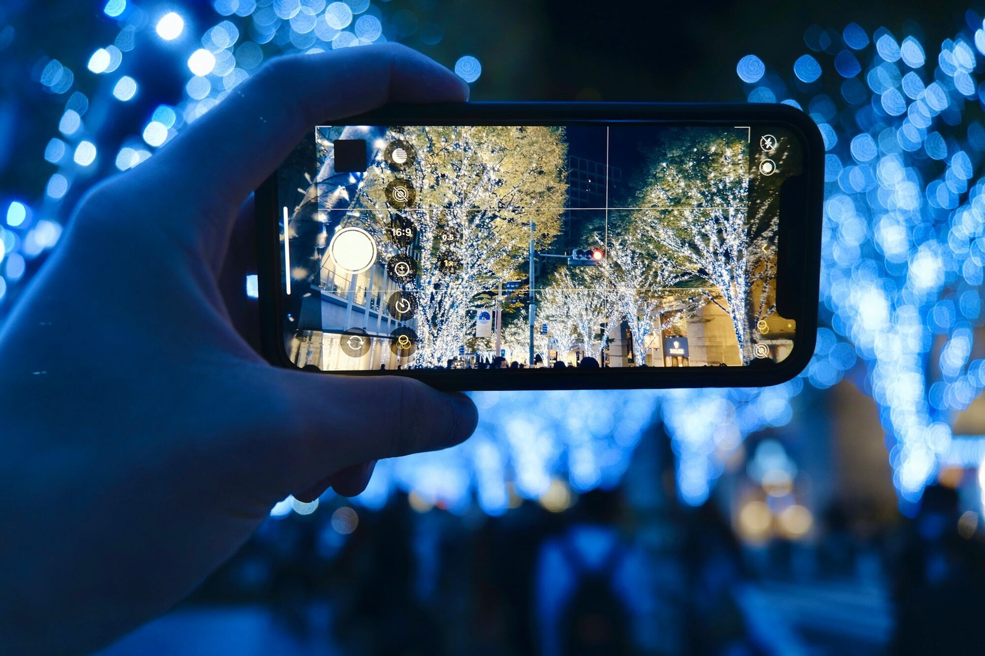 Person capturing illuminated trees at Roppongi Hills on smartphone at night