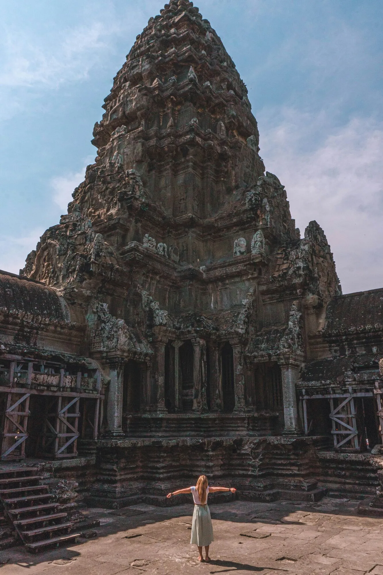 A woman standing with open arms in front of an ancient temple at Angkor Wat