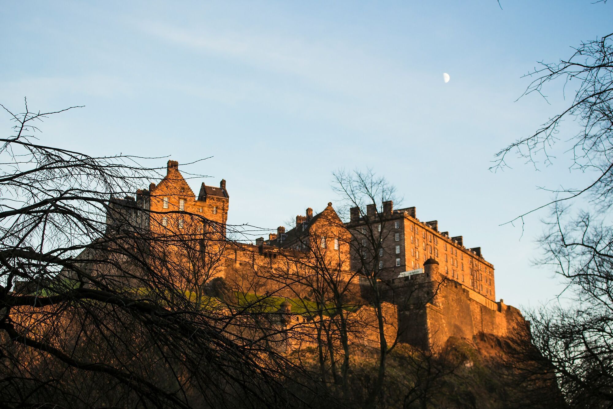 Edinburgh Castle at sunset with bare trees in the foreground