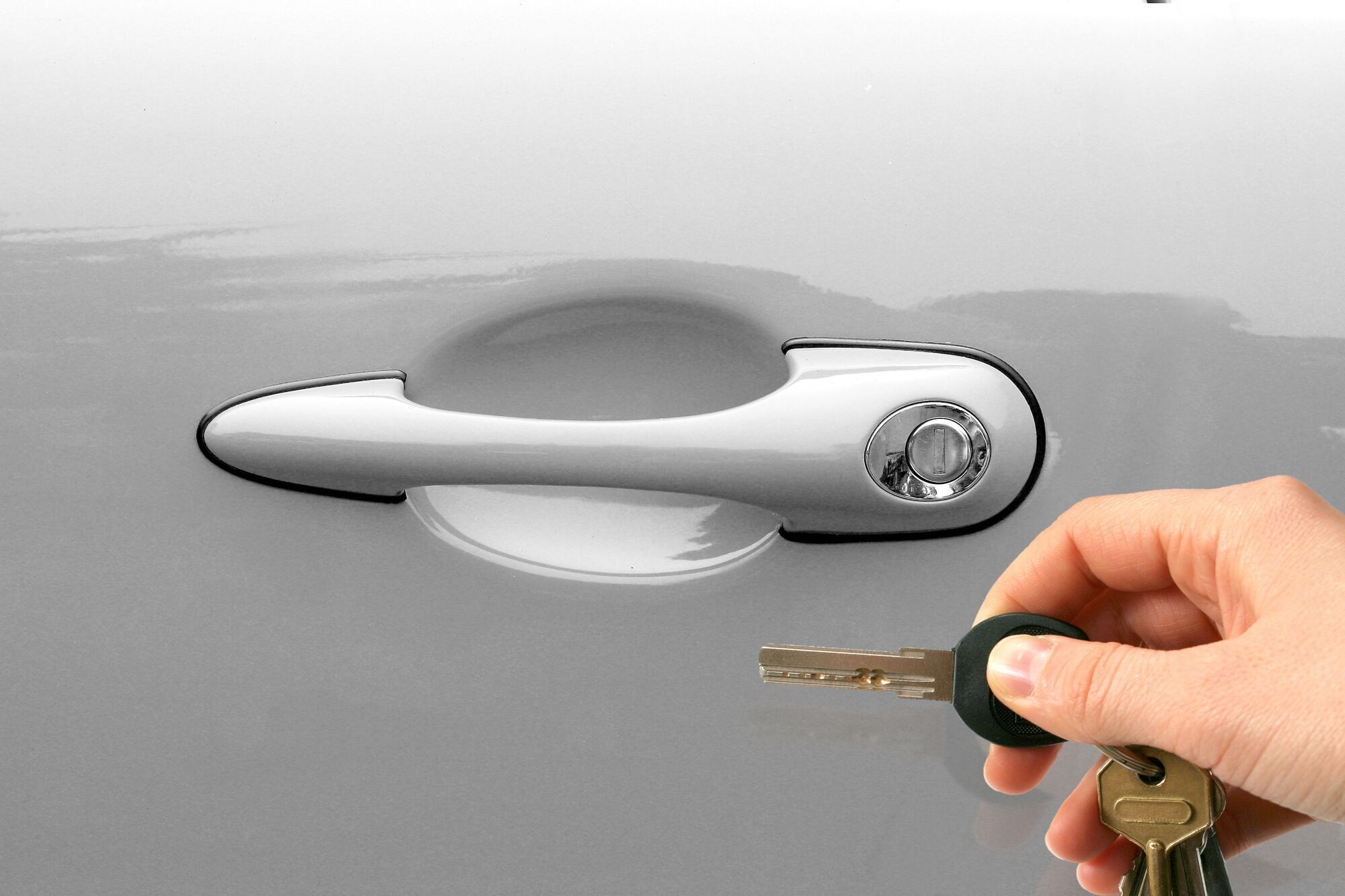 <span style="font-weight: 400;">Close-up of a hand holding a car key near the door handle of a silver vehicle, preparing to unlock it</span>