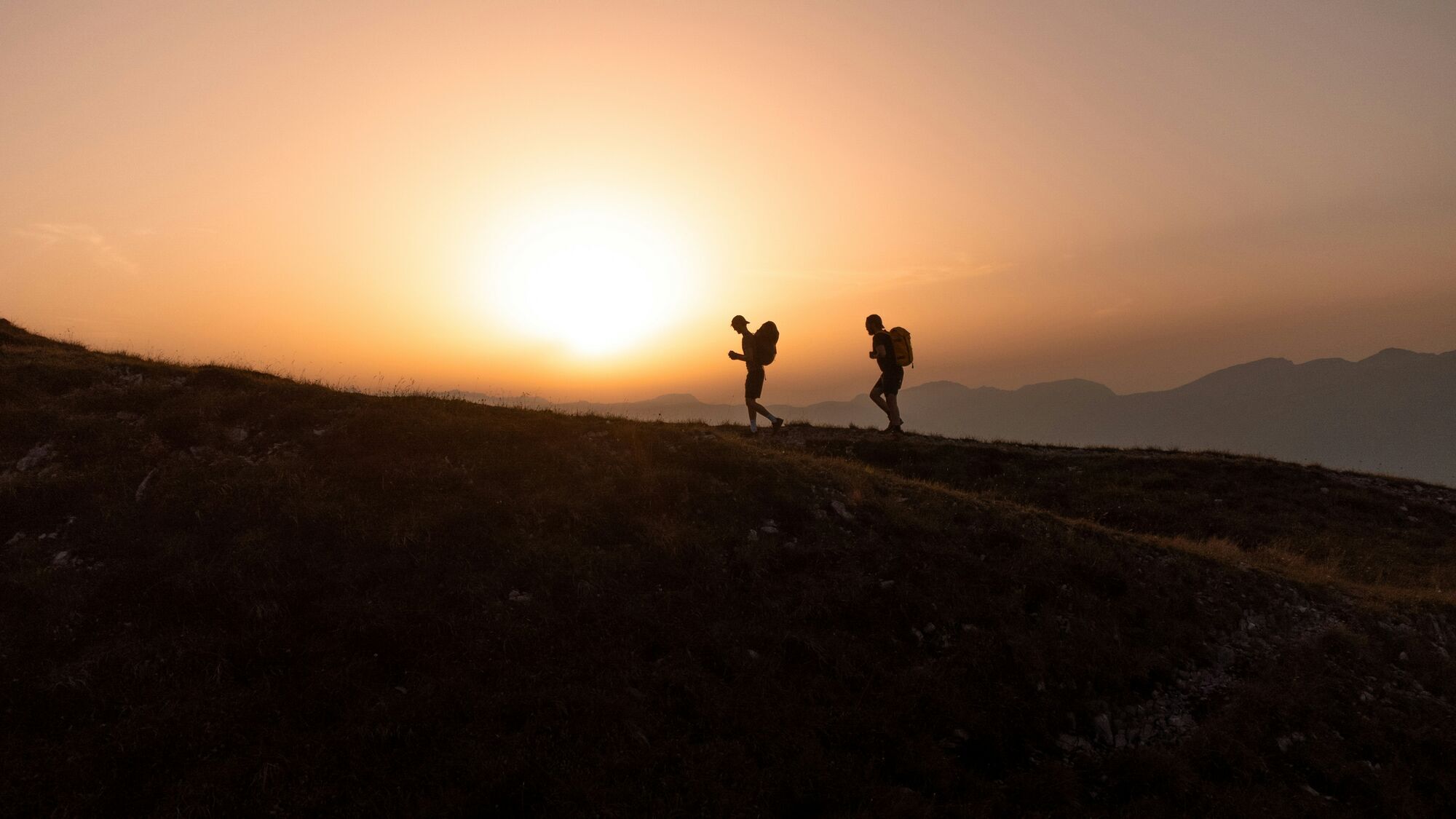 Two men walking along a ridge in the Swiss mountains while the sun is setting