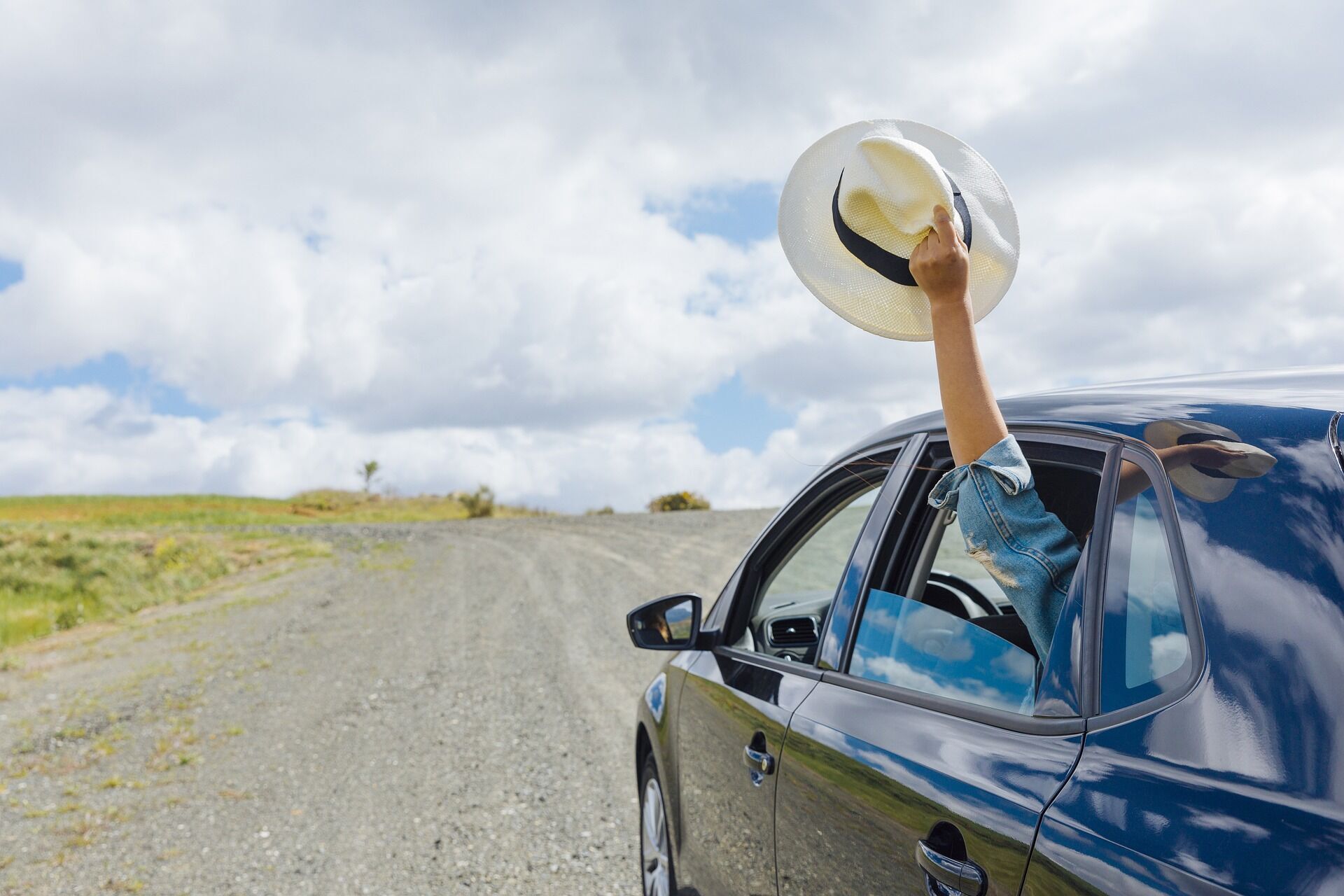 Person holding a hat out of a car window on a gravel road