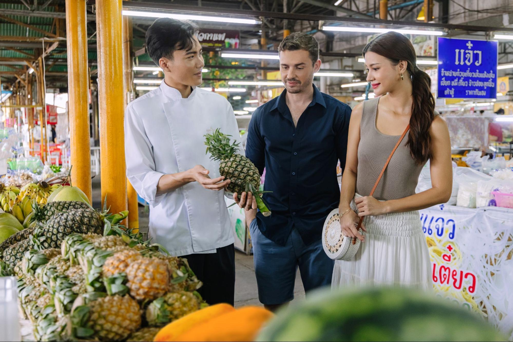 Chef showing a pineapple to two travelers at a local Thai market