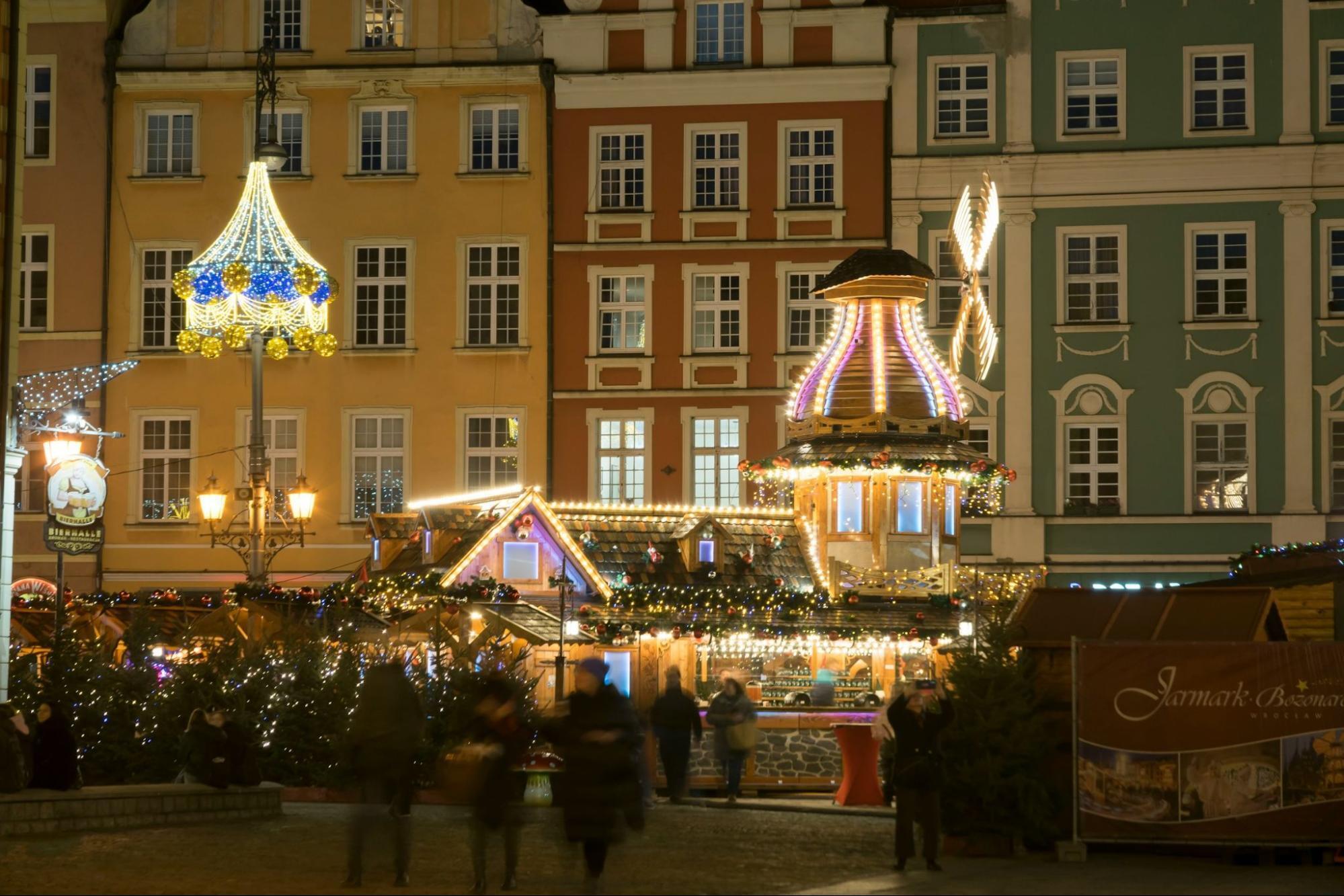 A brightly lit Christmas market with festive decorations and wooden stalls at night