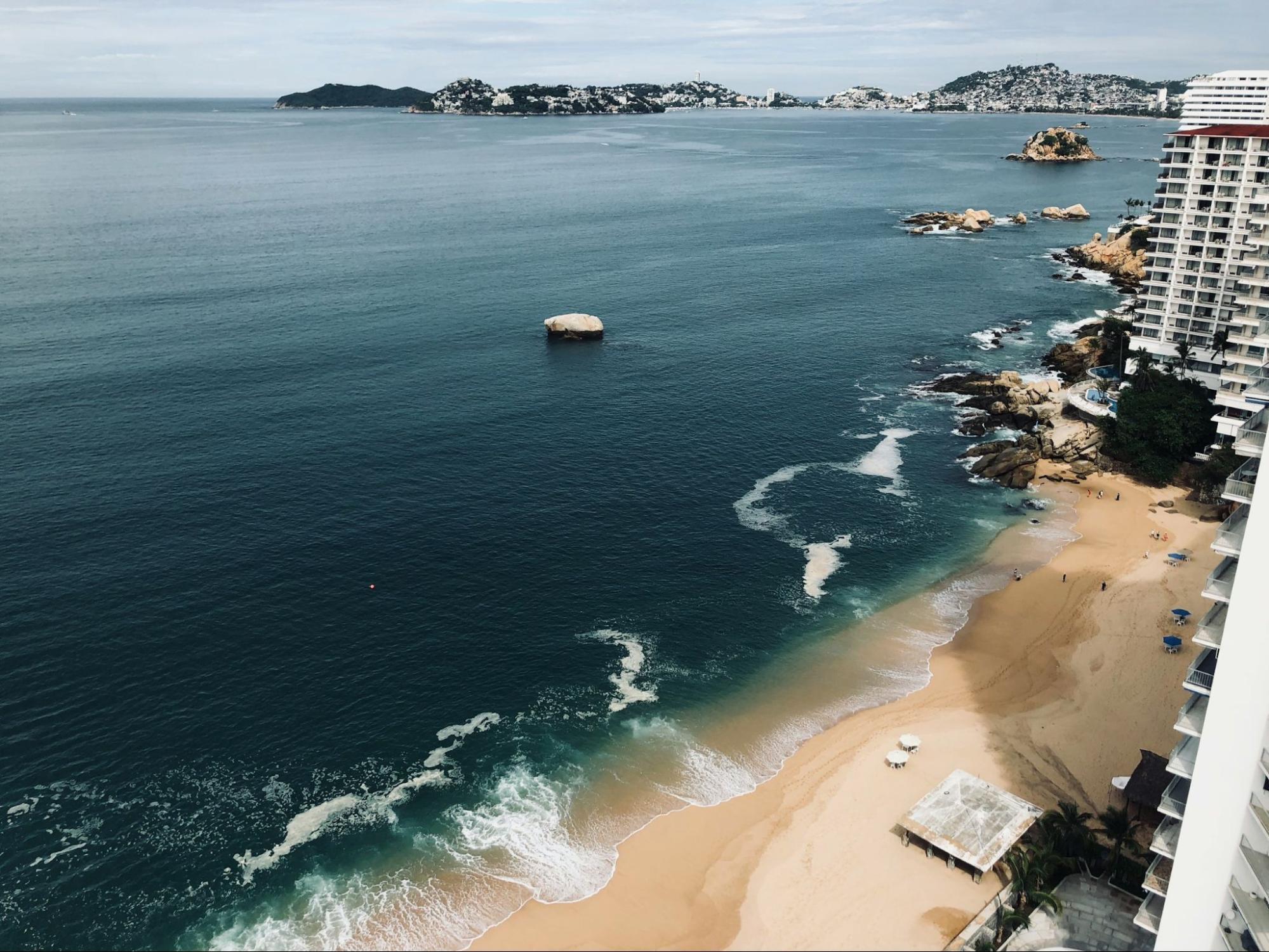 View of Acapulco’s sandy coastline with calm waves and coastal buildings
