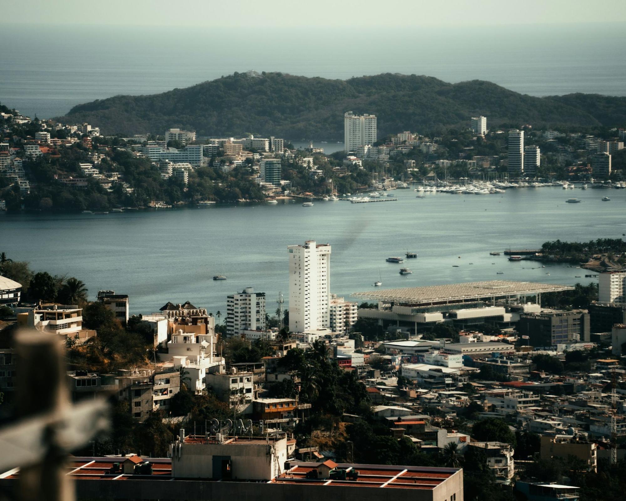 A panoramic view of Acapulco Bay with buildings, hills, and boats along the coast
