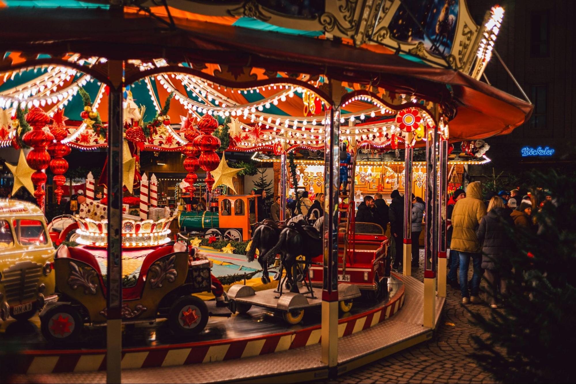 Colorful carousel and festive decorations at a Christmas market with people gathered around in the evening