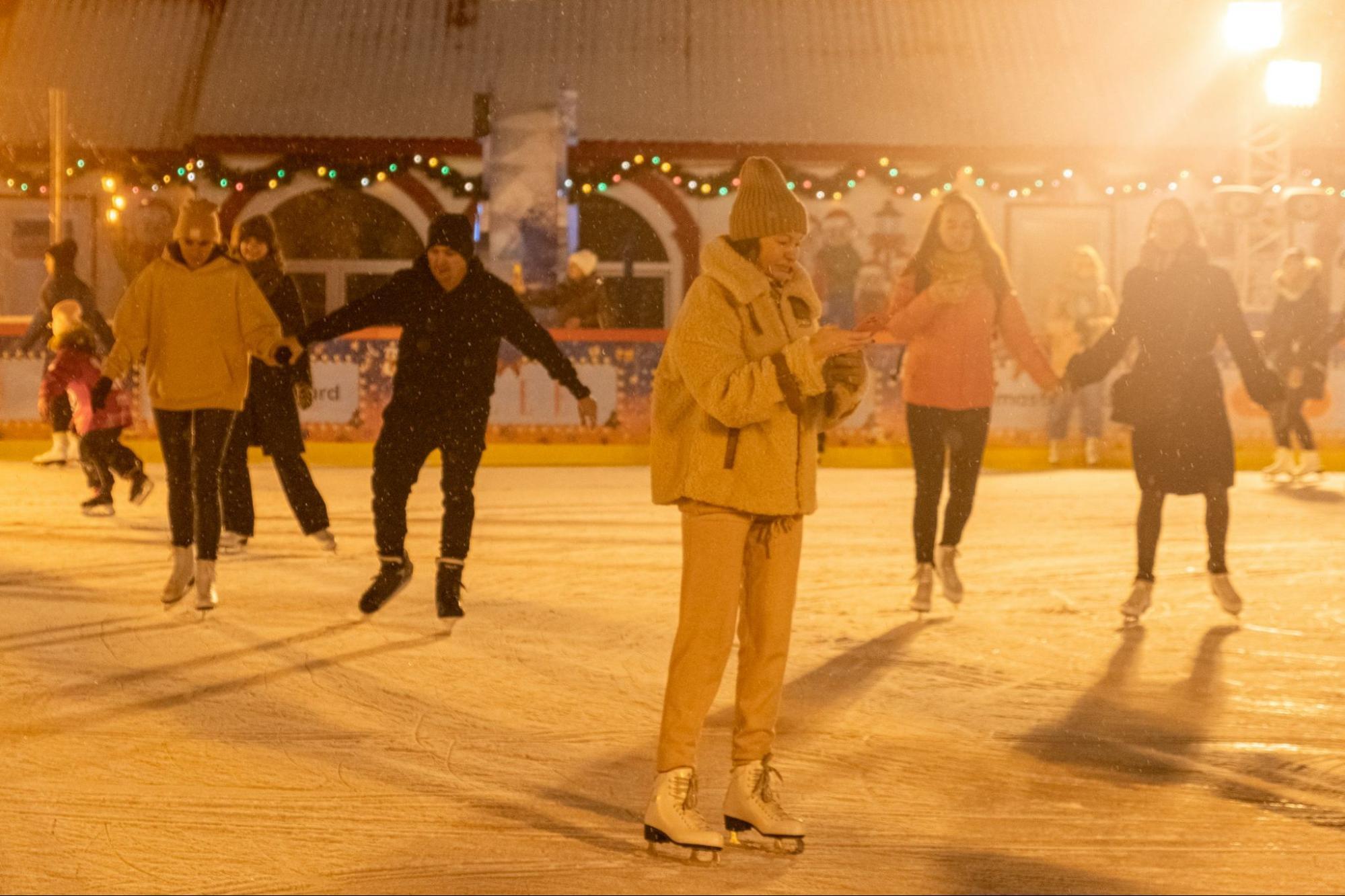 People ice skating at an outdoor winter rink under warm evening lights