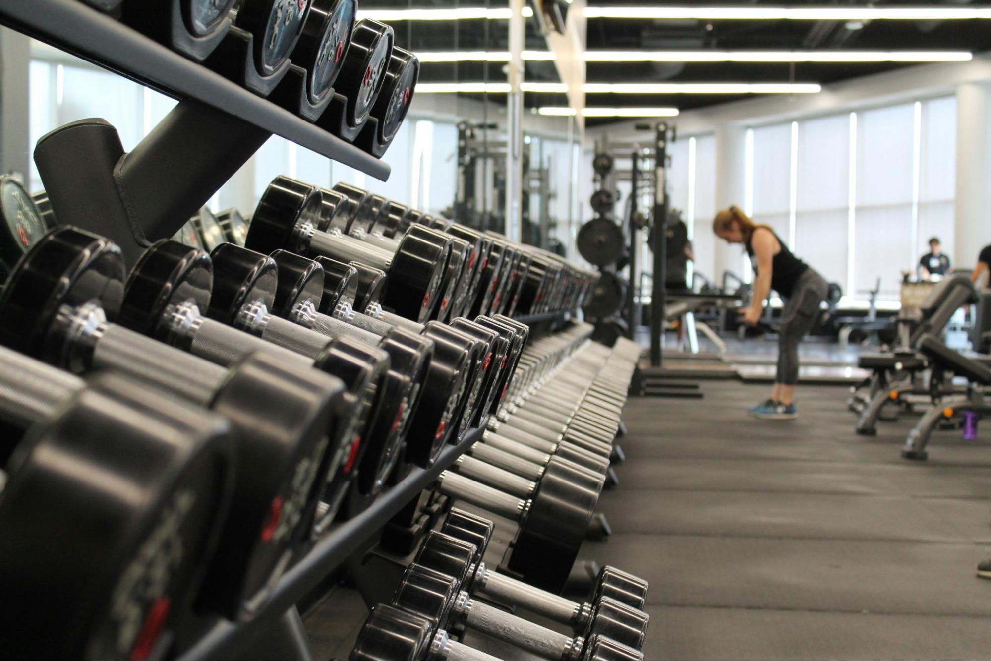 A fitness center with rows of dumbbells and people exercising