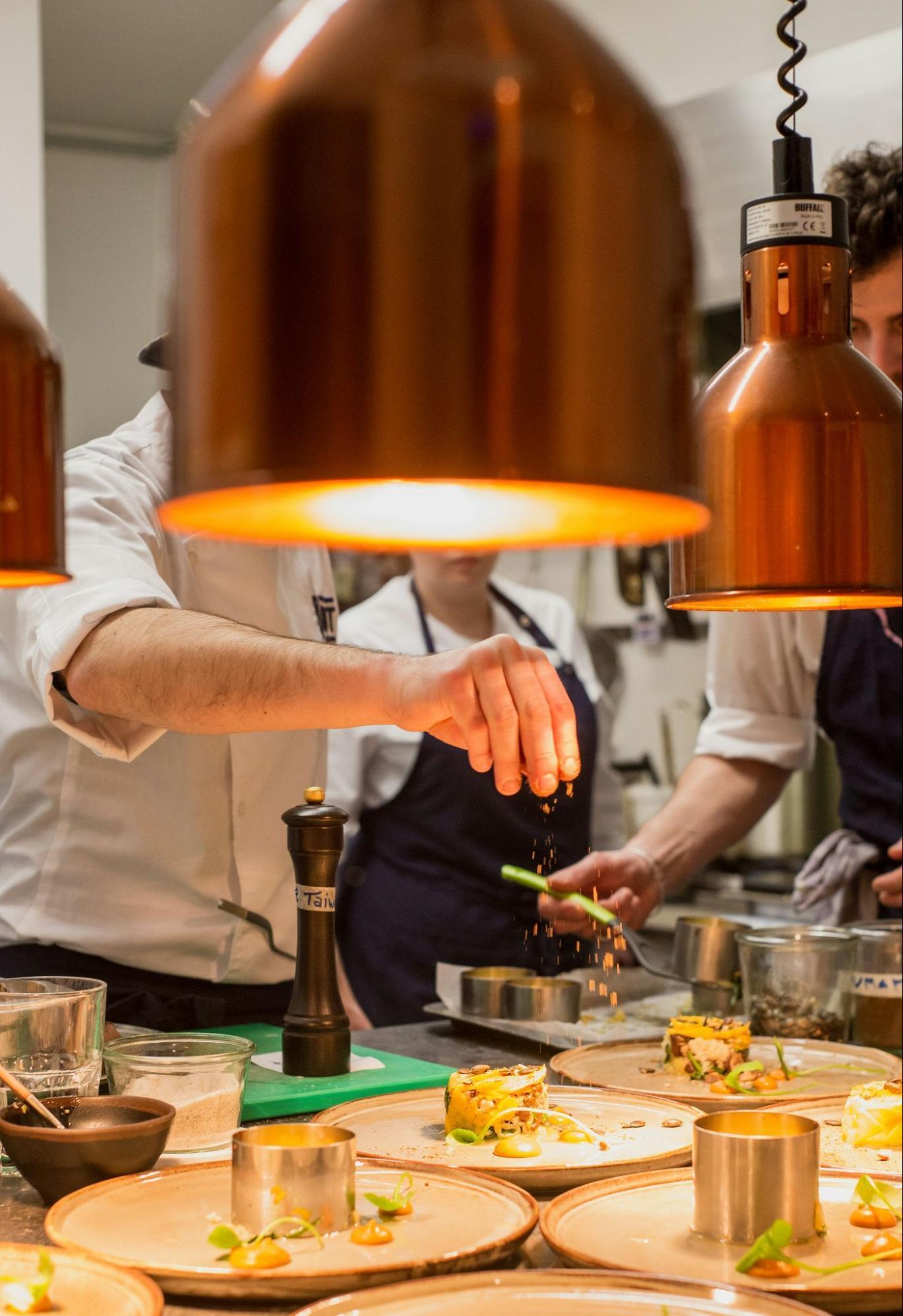 A chef garnishing dishes in a professional kitchen under warm lights