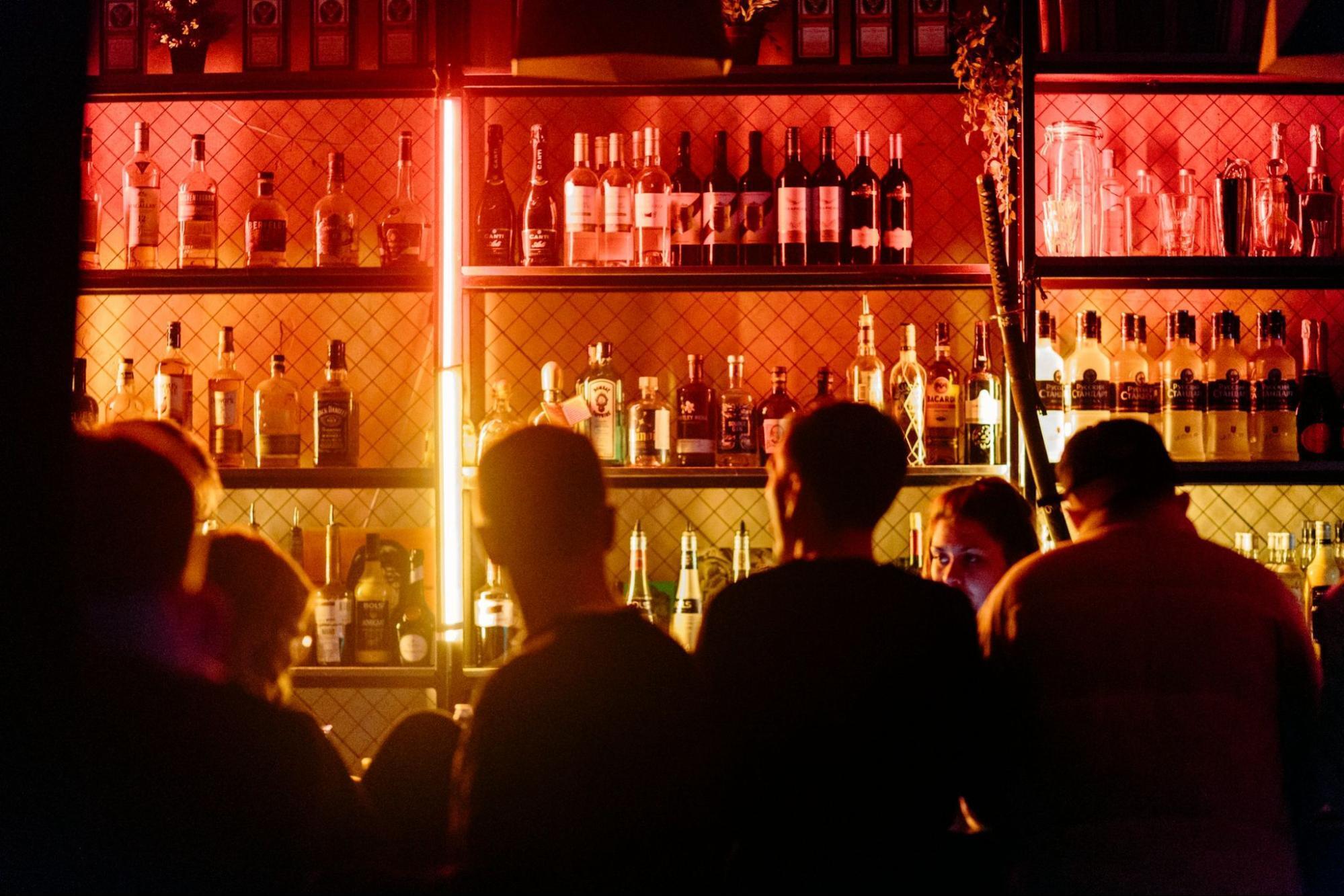 People standing at a dimly lit bar with bottles on shelves