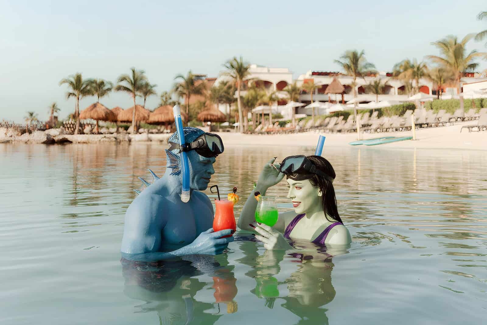 Two people in Halloween costumes snorkeling and holding colorful drinks in the Caribbean Sea