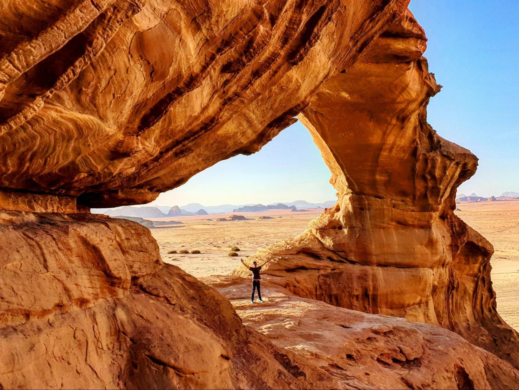 Traveler standing under natural rock arch in Wadi Rum desert