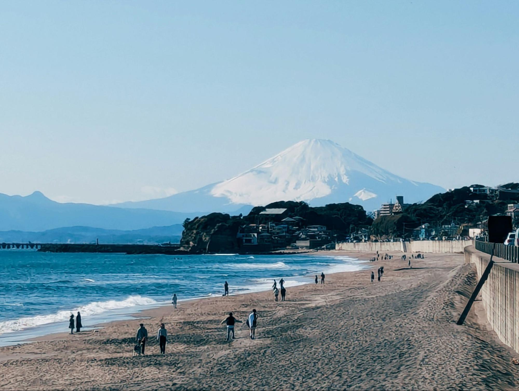 Beachgoers walking along the shore with Mount Fuji visible in the background