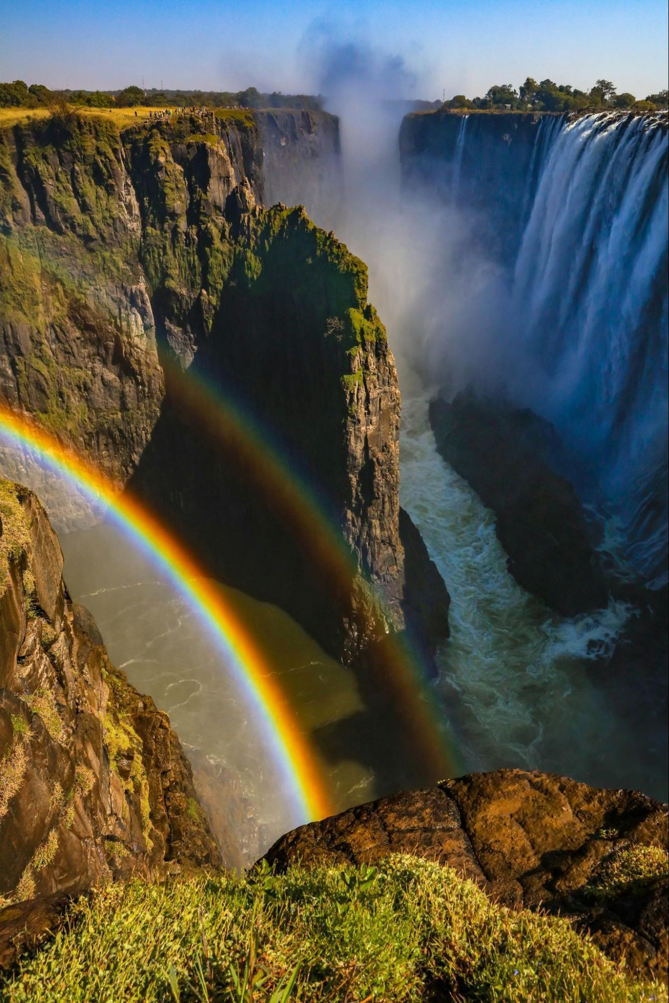 View of Victoria Falls in Zambia with a double rainbow forming above the gorge on a sunny day