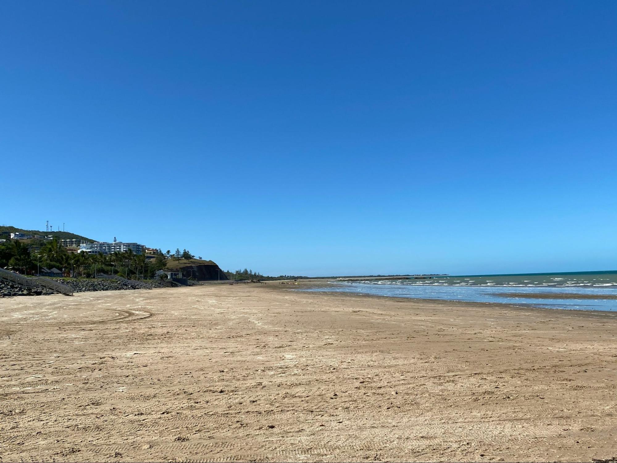 Sunny empty beach with calm waves and clear blue sky