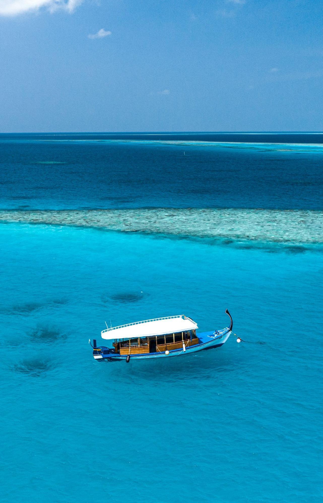Traditional Maldivian dhoni boat floating on clear turquoise water near a coral reef