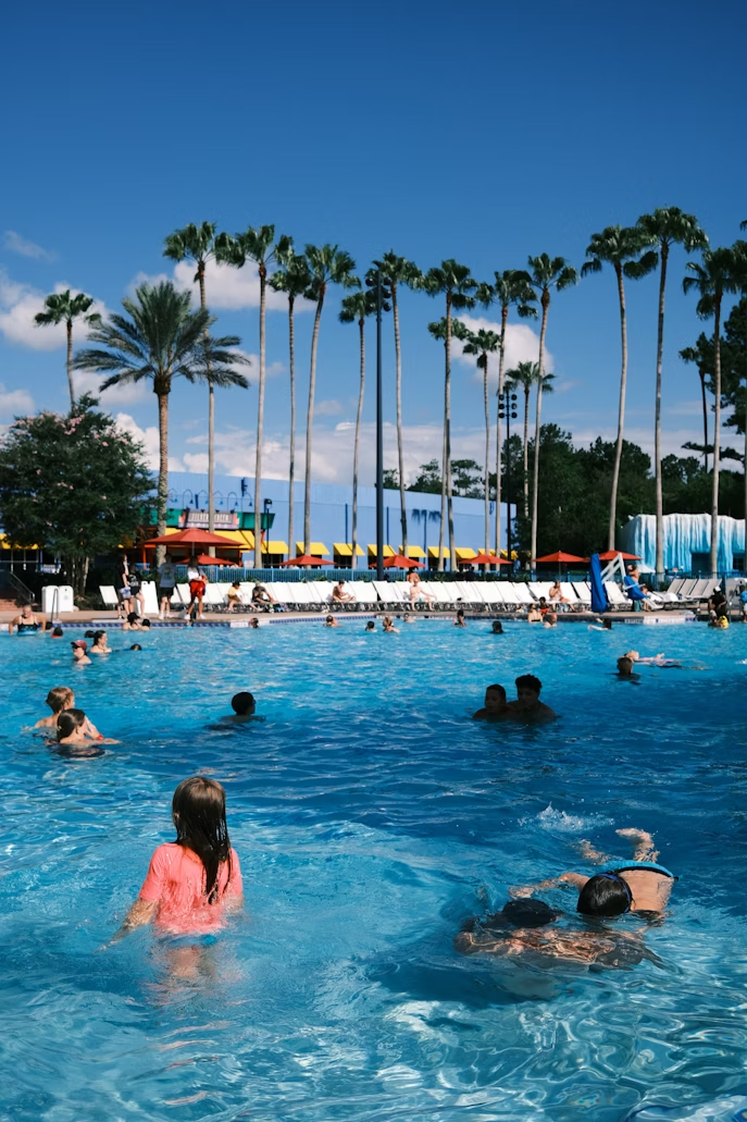People enjoying a sunny day at a water park pool surrounded by tall palm trees