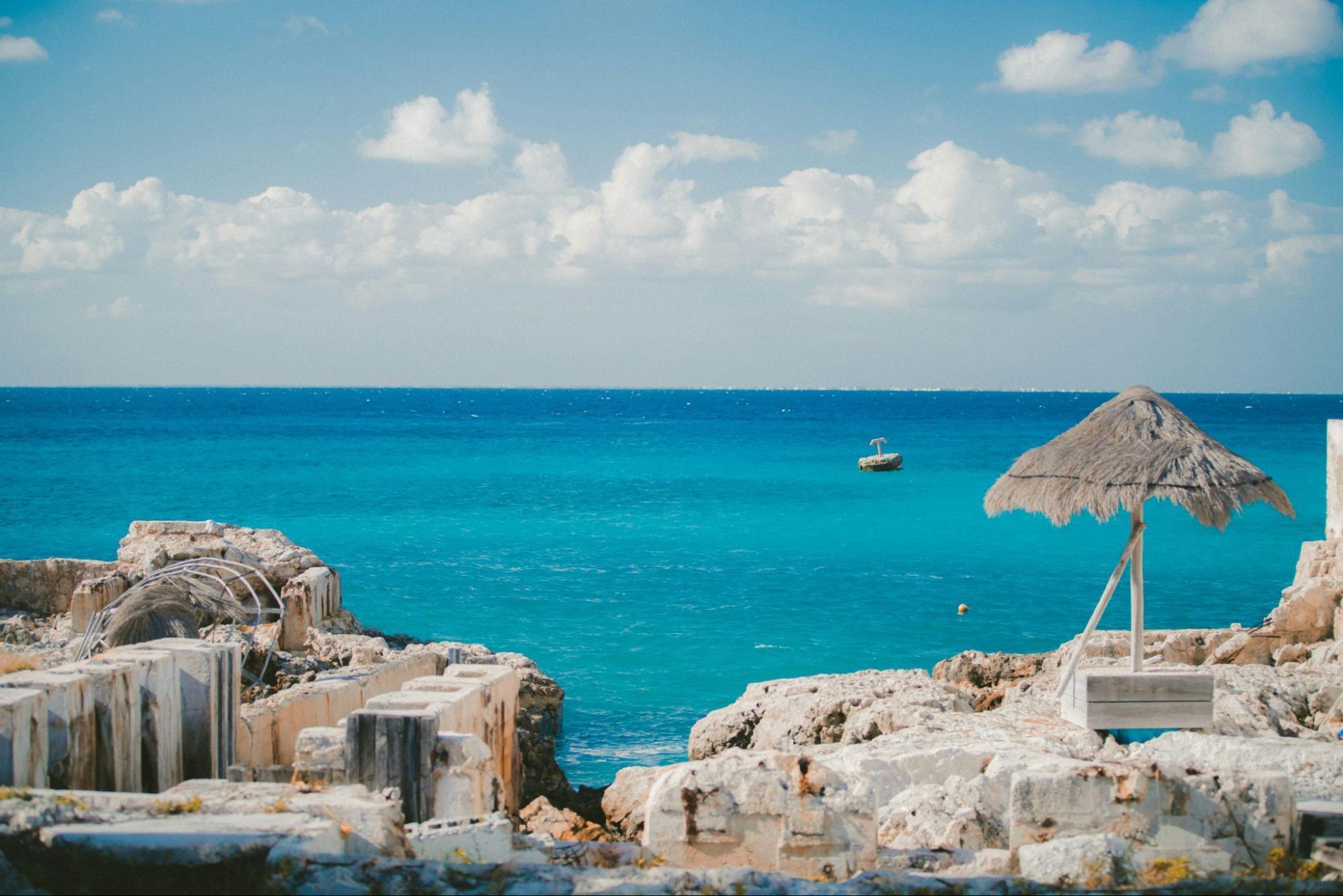 Rocky Caribbean coastline with turquoise sea and thatched parasol
