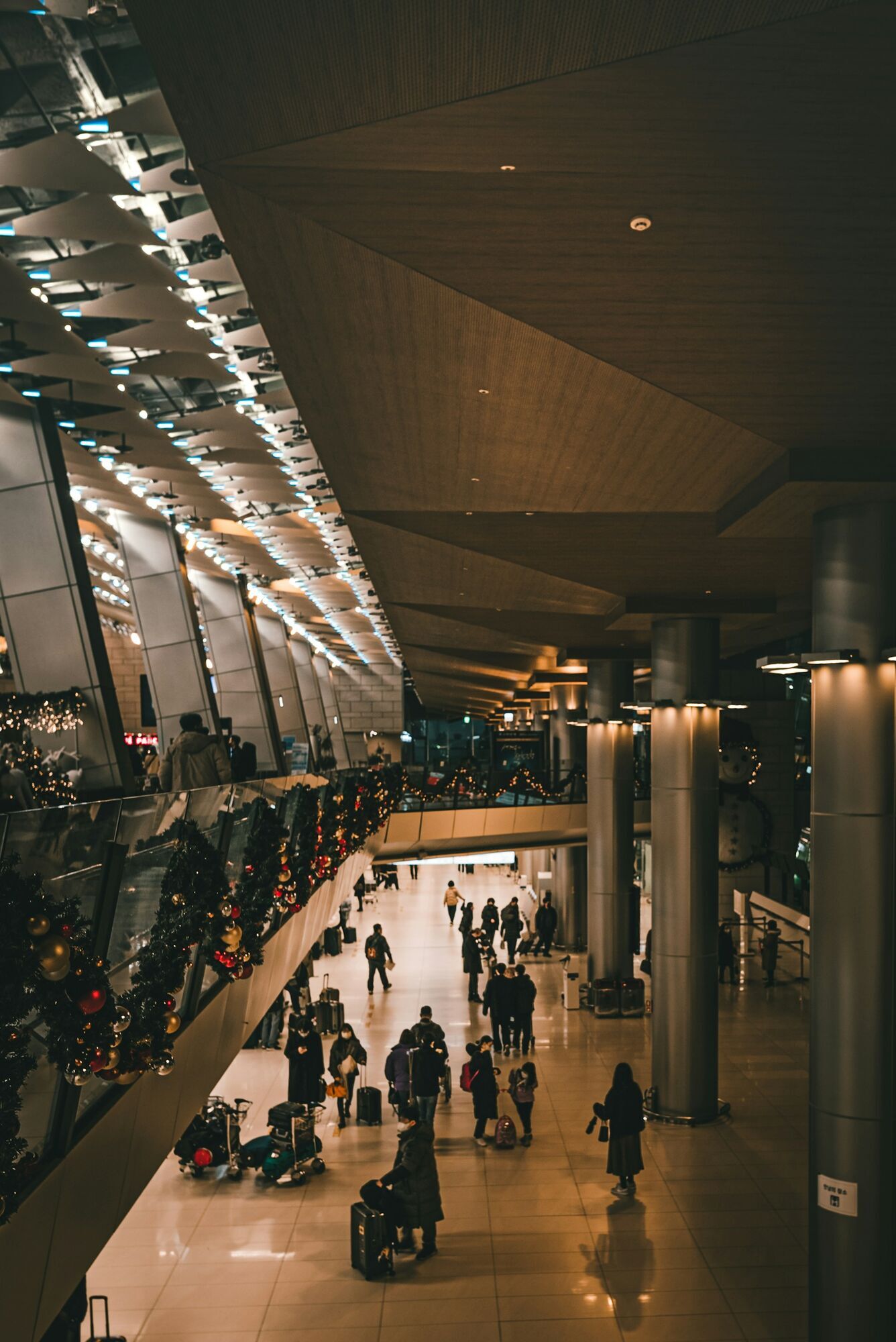 People with luggage walk through an illuminated airport terminal decorated for the holidays