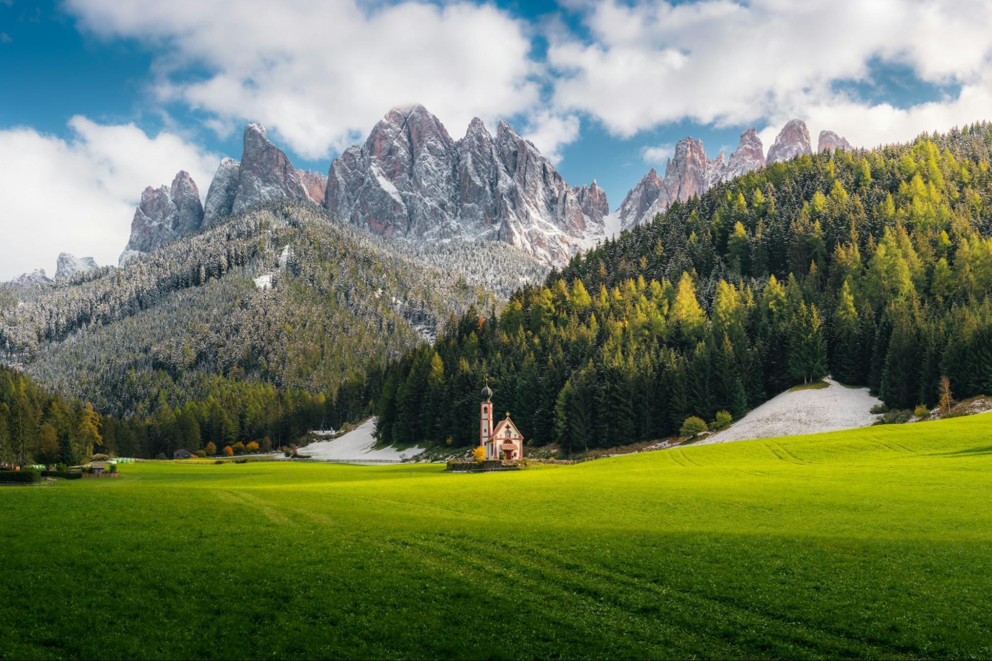 Scenic valley in the Dolomites with a small church and snow-dusted mountains