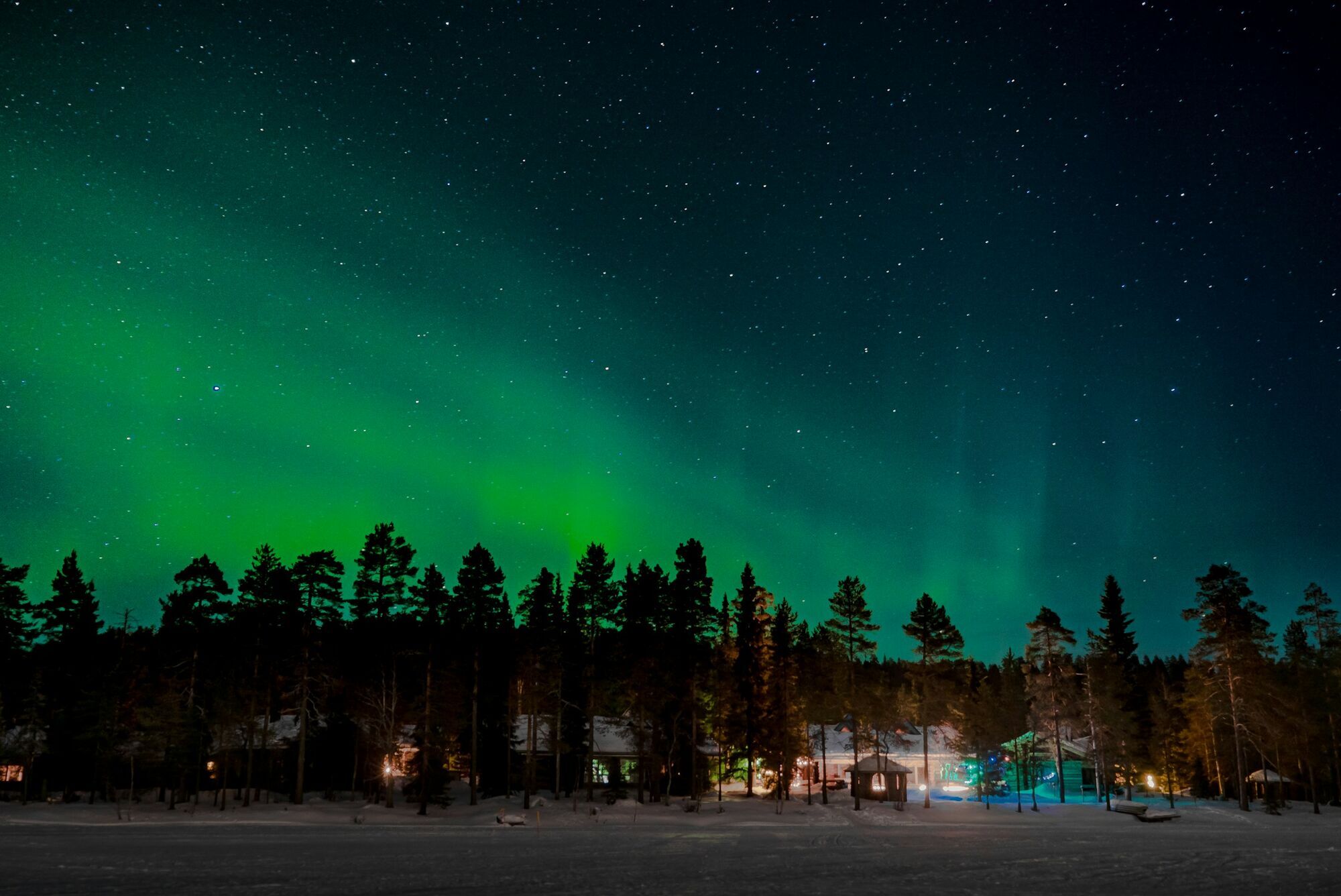 Northern lights glowing above snowy Lapland cabins