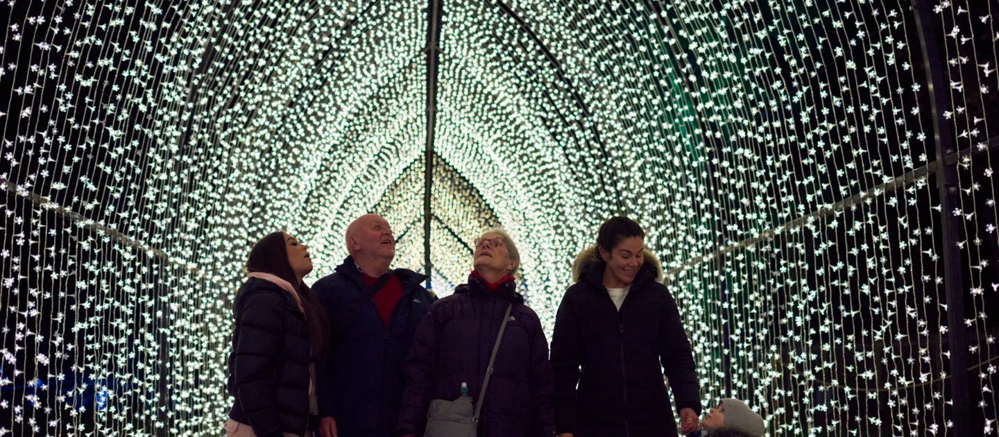 A family walks through a tunnel of sparkling lights at Dunham Massey’s Christmas trail