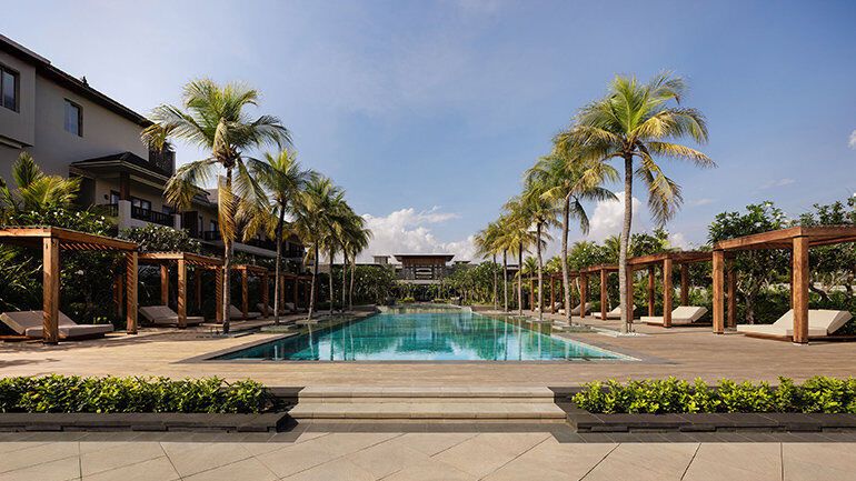 Outdoor pool area with palm trees and wooden cabanas
