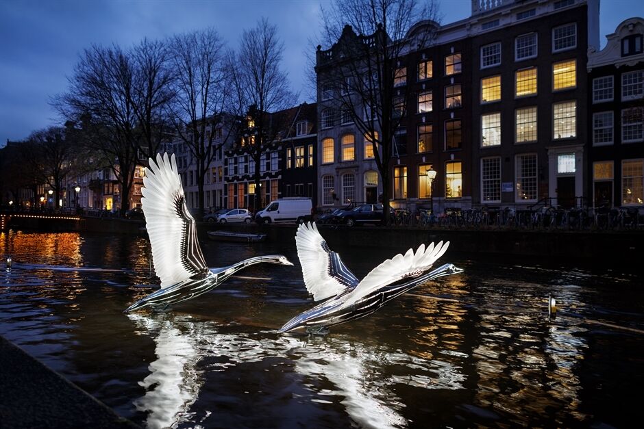 Illuminated swan sculptures floating on an Amsterdam canal at dusk