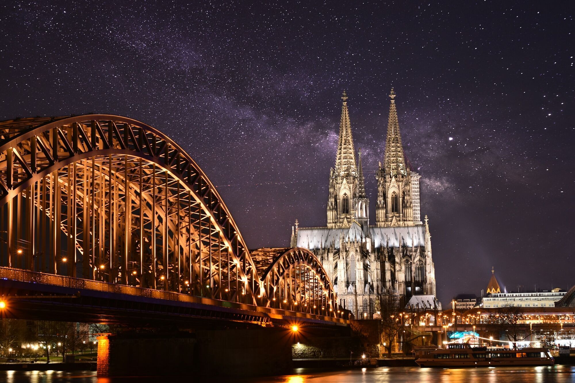 Cologne Cathedral and Hohenzollern Bridge illuminated at night under a starry sky