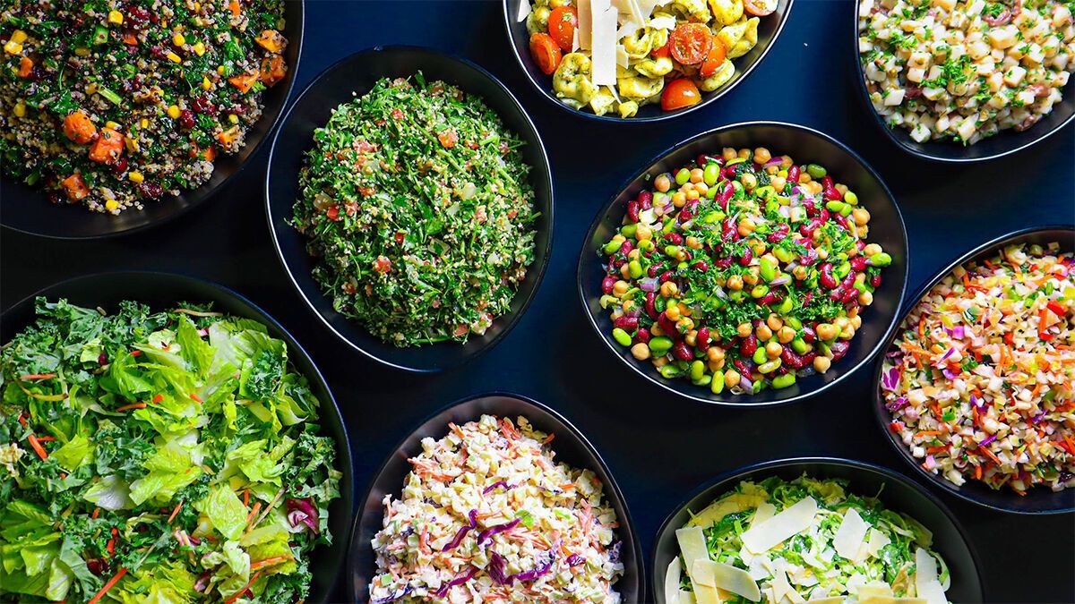 A variety of fresh salads in black bowls, featuring mixed greens, legumes, and grains