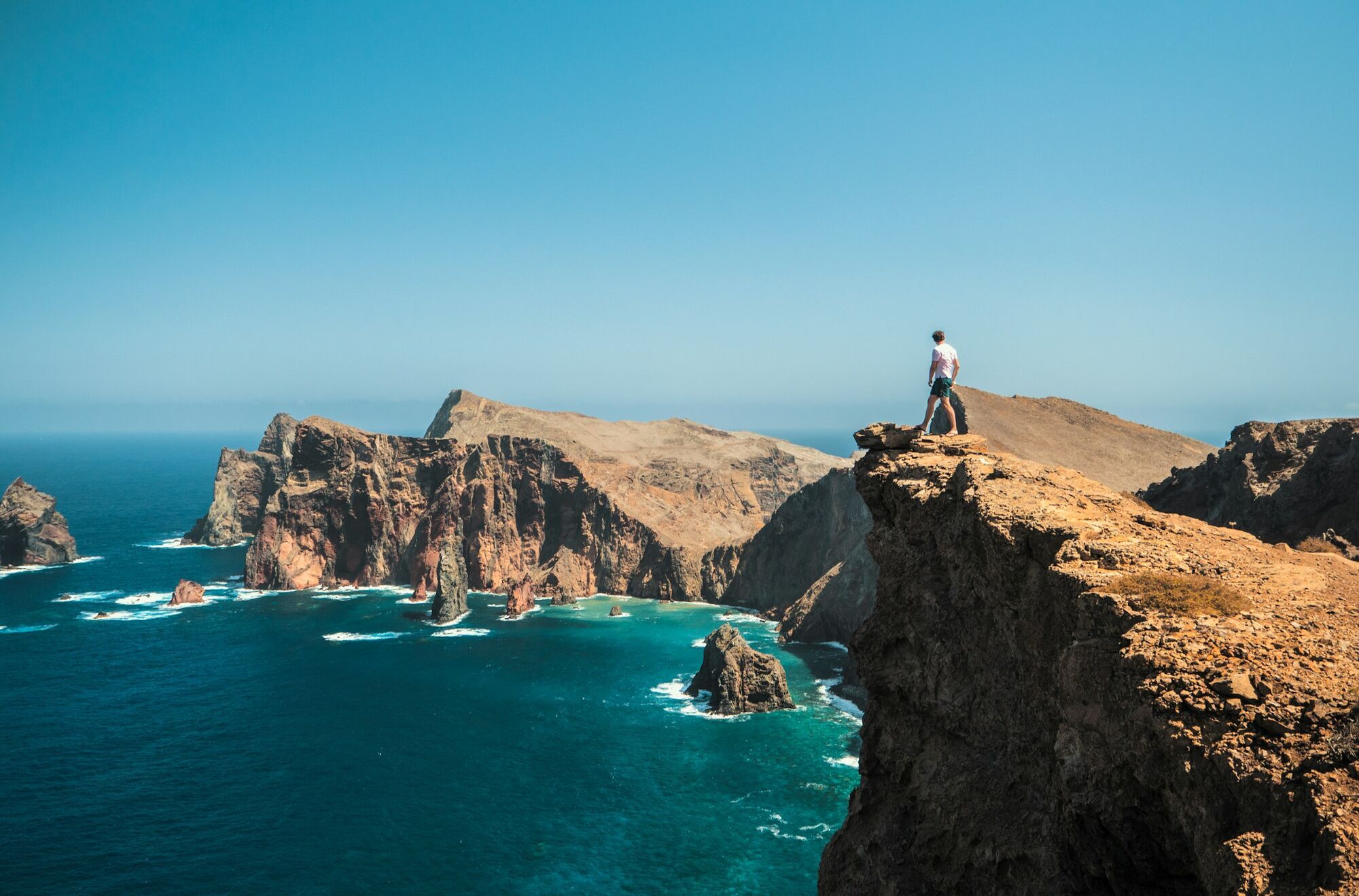 A traveler standing on a cliff overlooking the rugged coastline and blue ocean of Madeira, Portugal