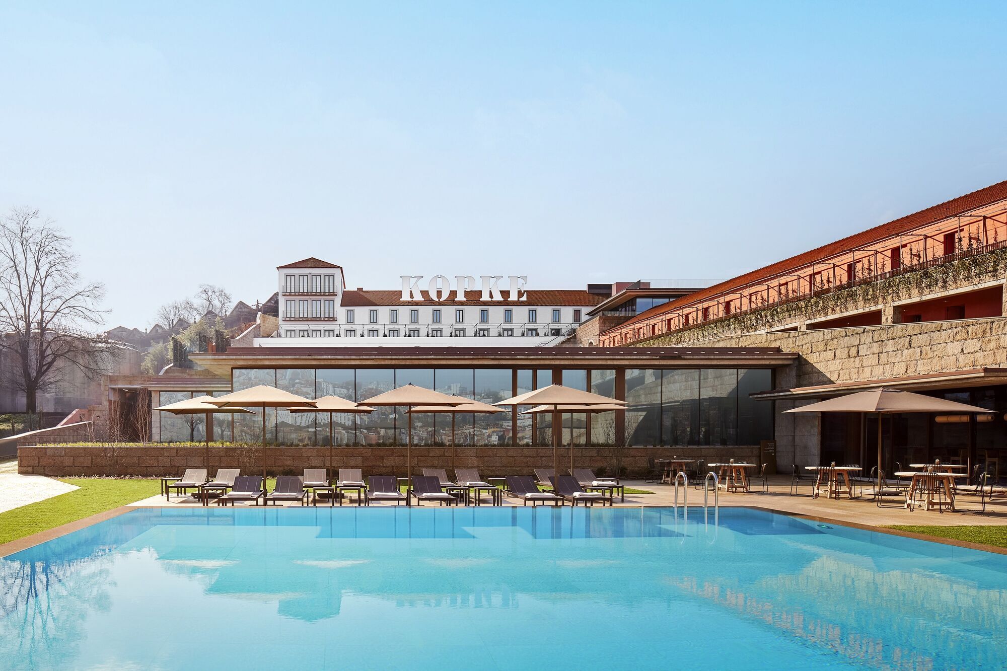 Outdoor pool area of Tivoli Kopke Porto Gaia Hotel with sun loungers and umbrellas, set against the backdrop of historic wine cellars