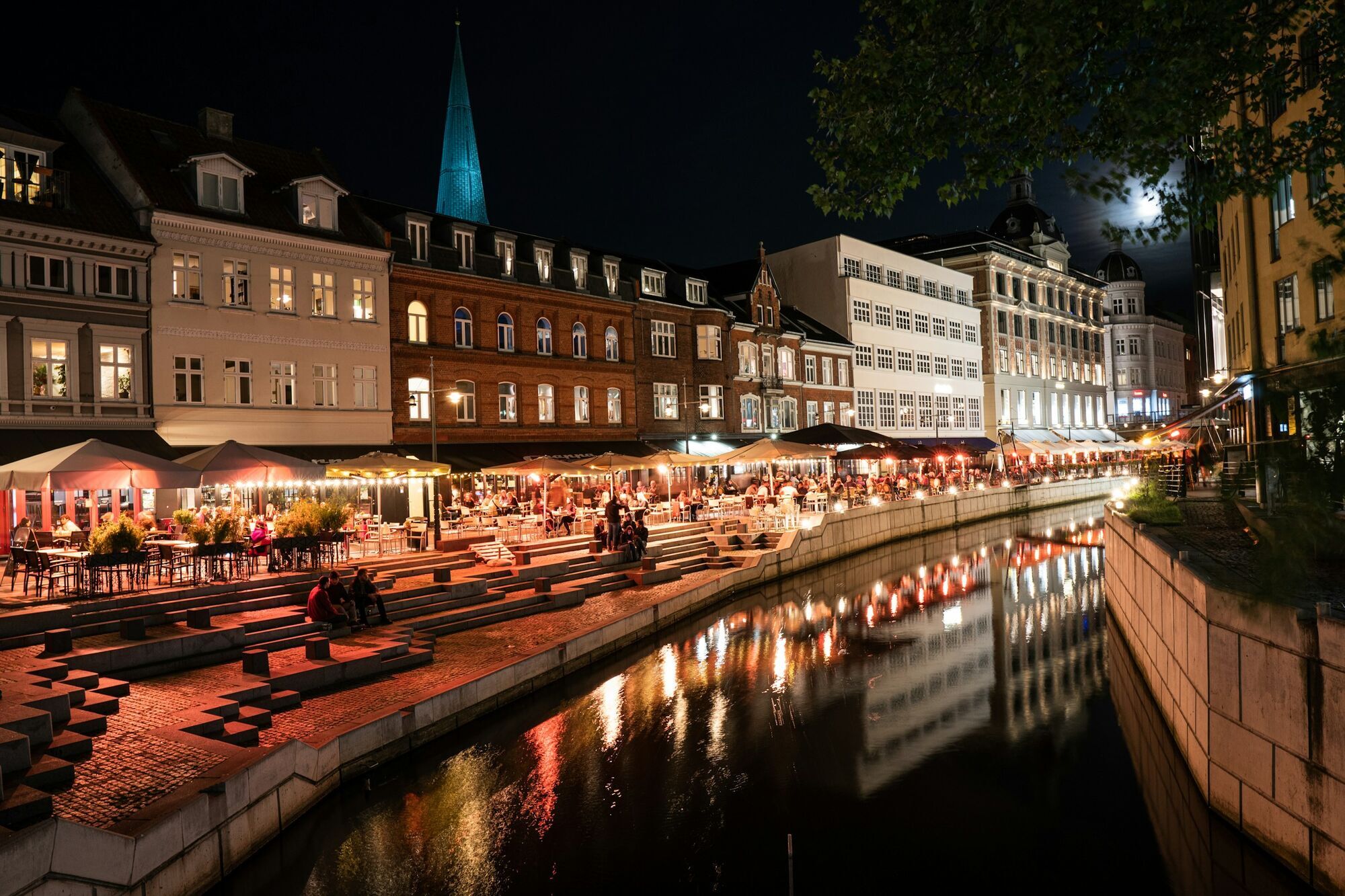 A lively riverside dining scene in Aarhus, Denmark, illuminated at night