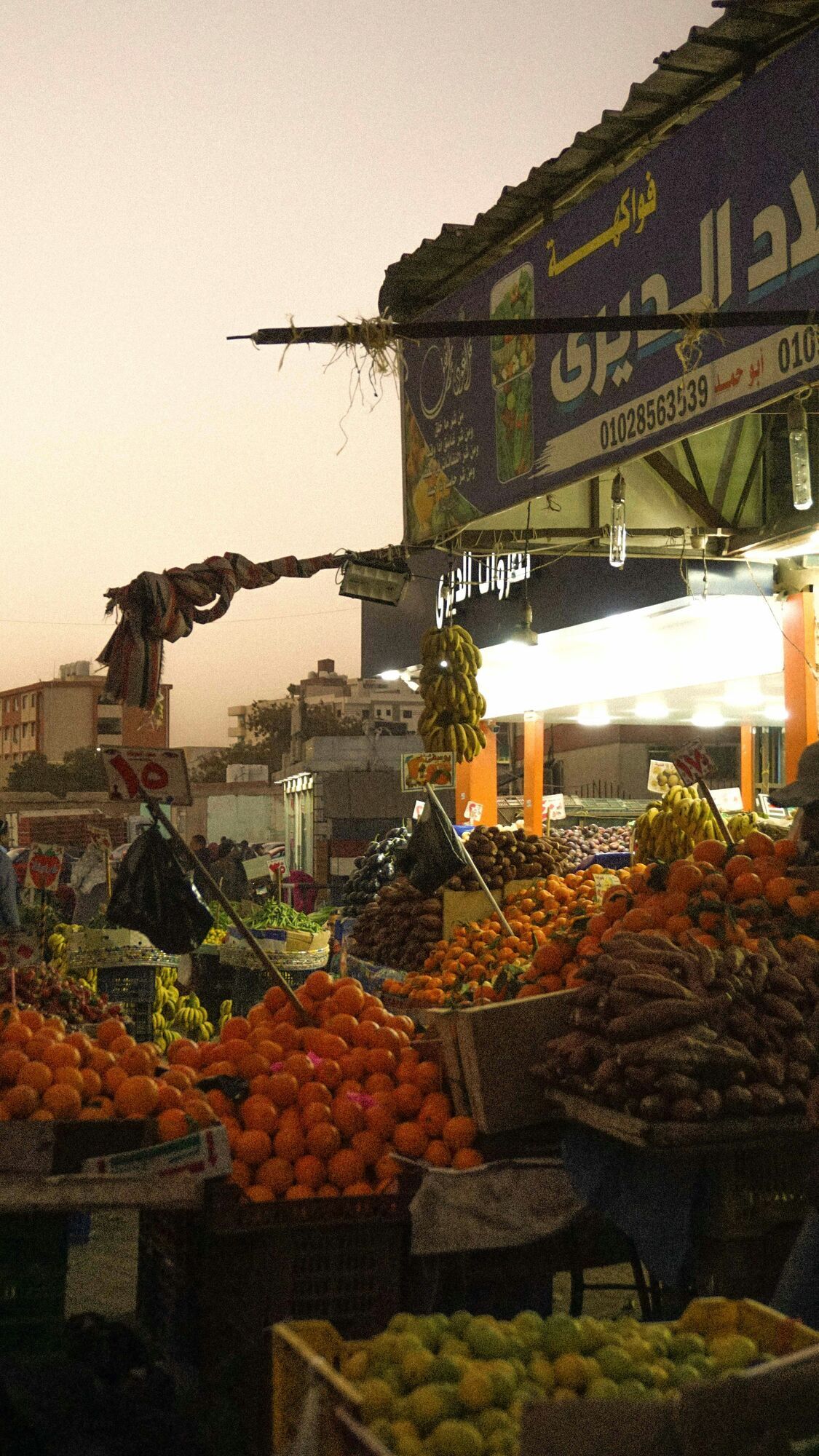 A bustling evening market in Hurghada, Egypt, with fresh fruits and vegetables displayed under bright lights