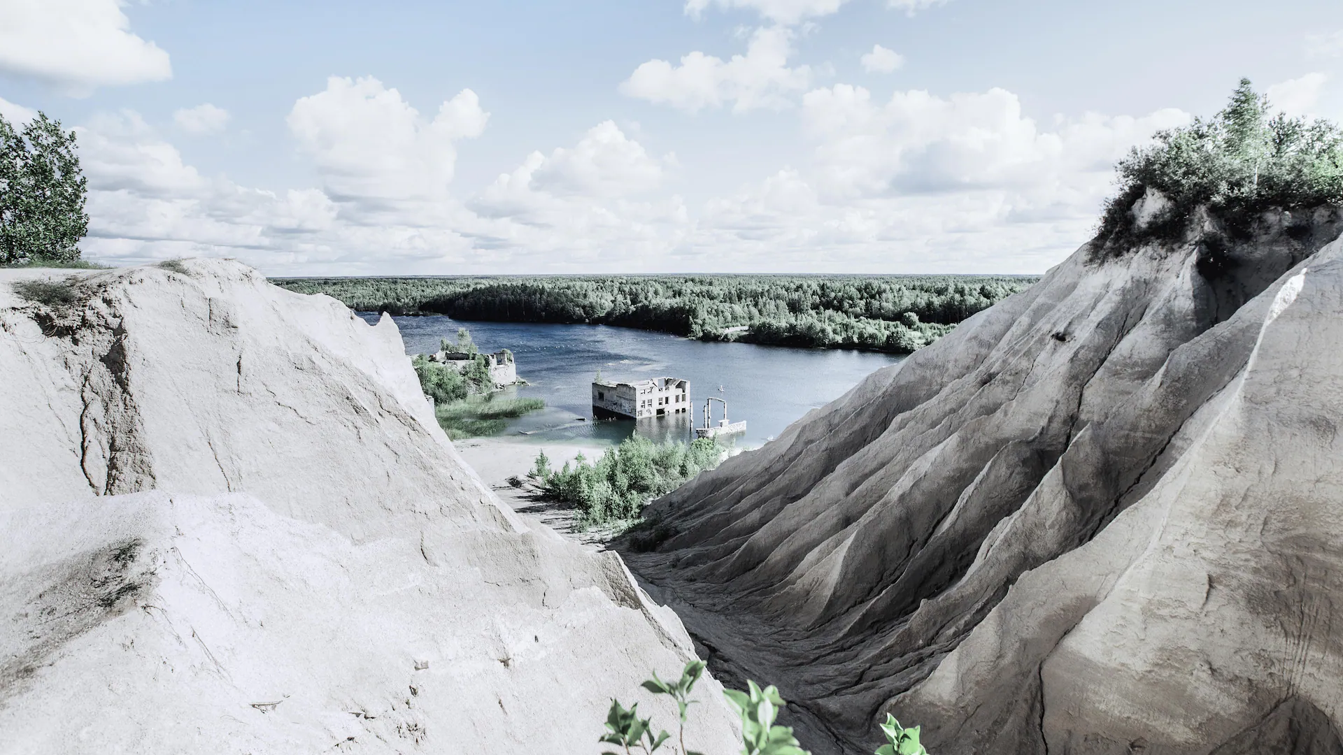Rummu quarry with submerged building, sandy hills, and forest in the background