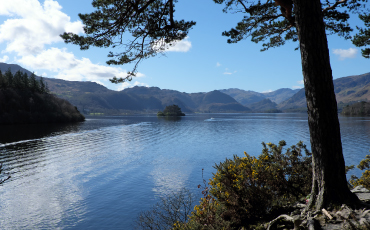 View of Derwentwater from Friar’s Crag with surrounding hills and trees under a blue sky