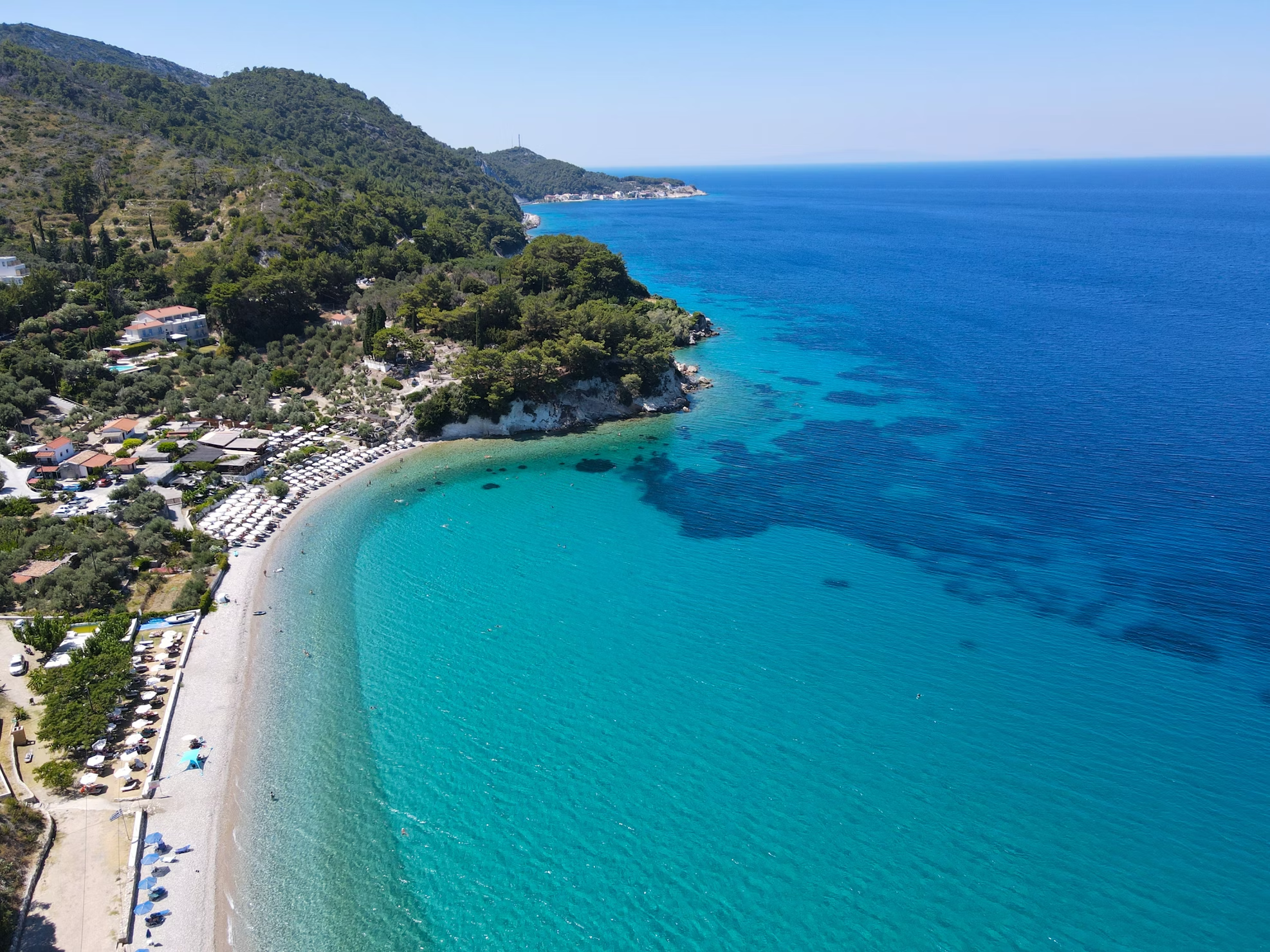 Aerial view of Tsamadou Beach with turquoise waters and forested hills on Samos Island, Greece