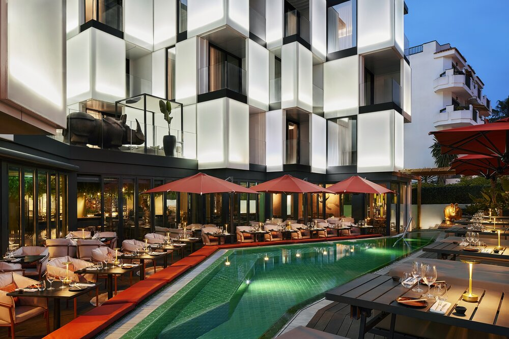 Modern NH Collection hotel in Ibiza with illuminated facade and a poolside dining area at dusk
