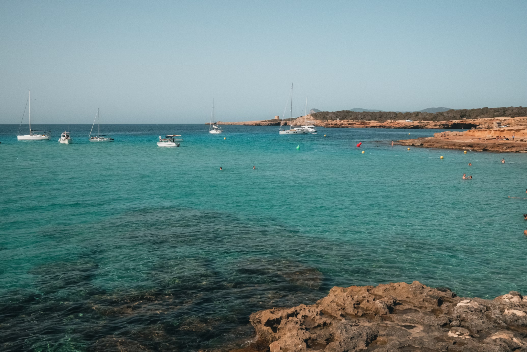 Clear turquoise waters with anchored sailboats near a rocky coastline in Ibiza