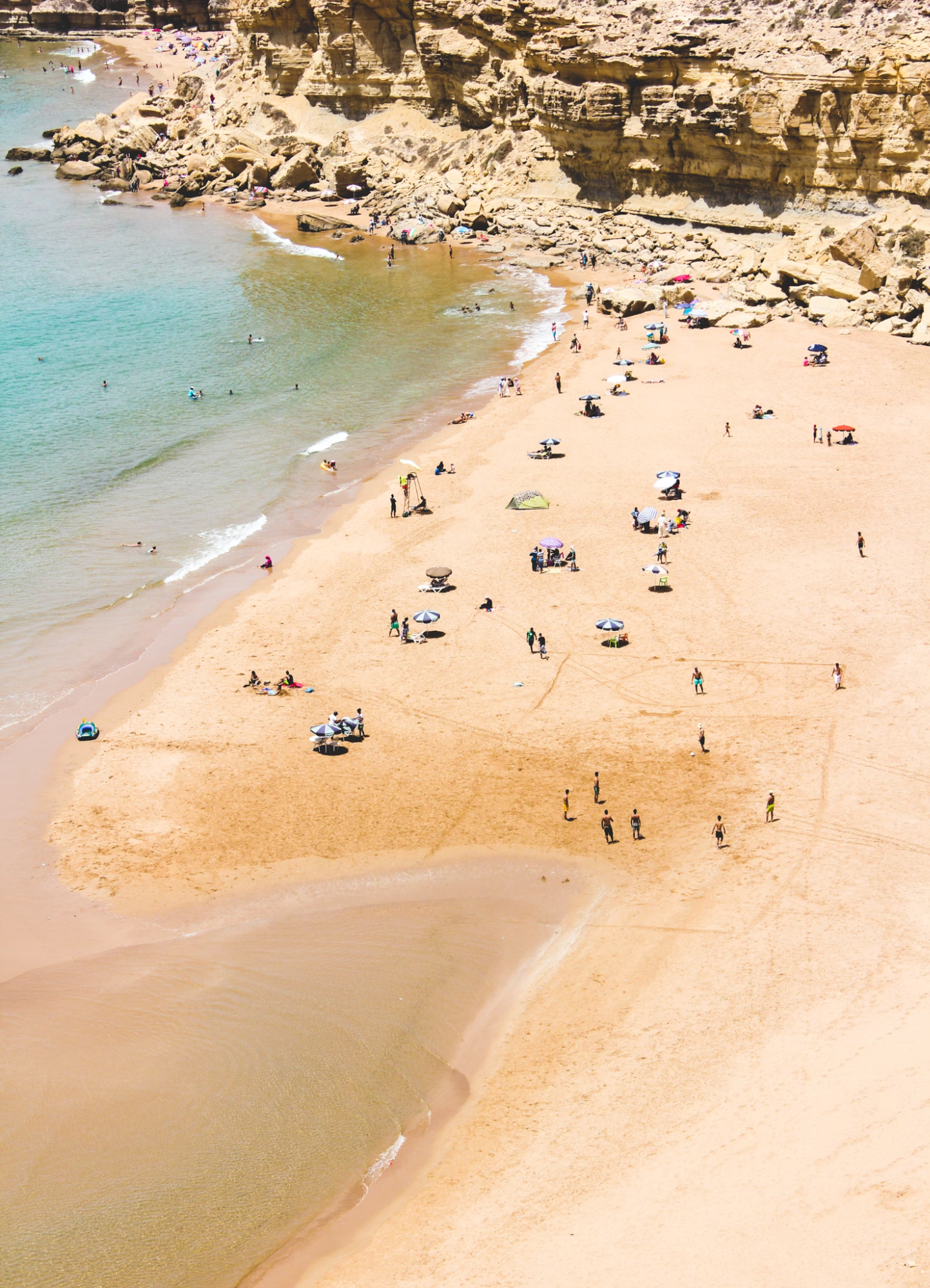 People on a sandy beach in Agadir with rocky cliffs in the background