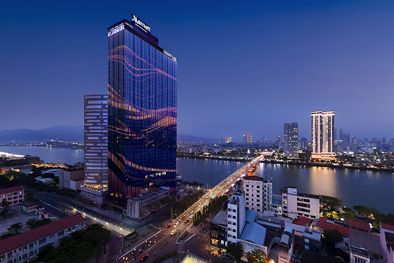 Tall glass hotel building near river in Danang at night