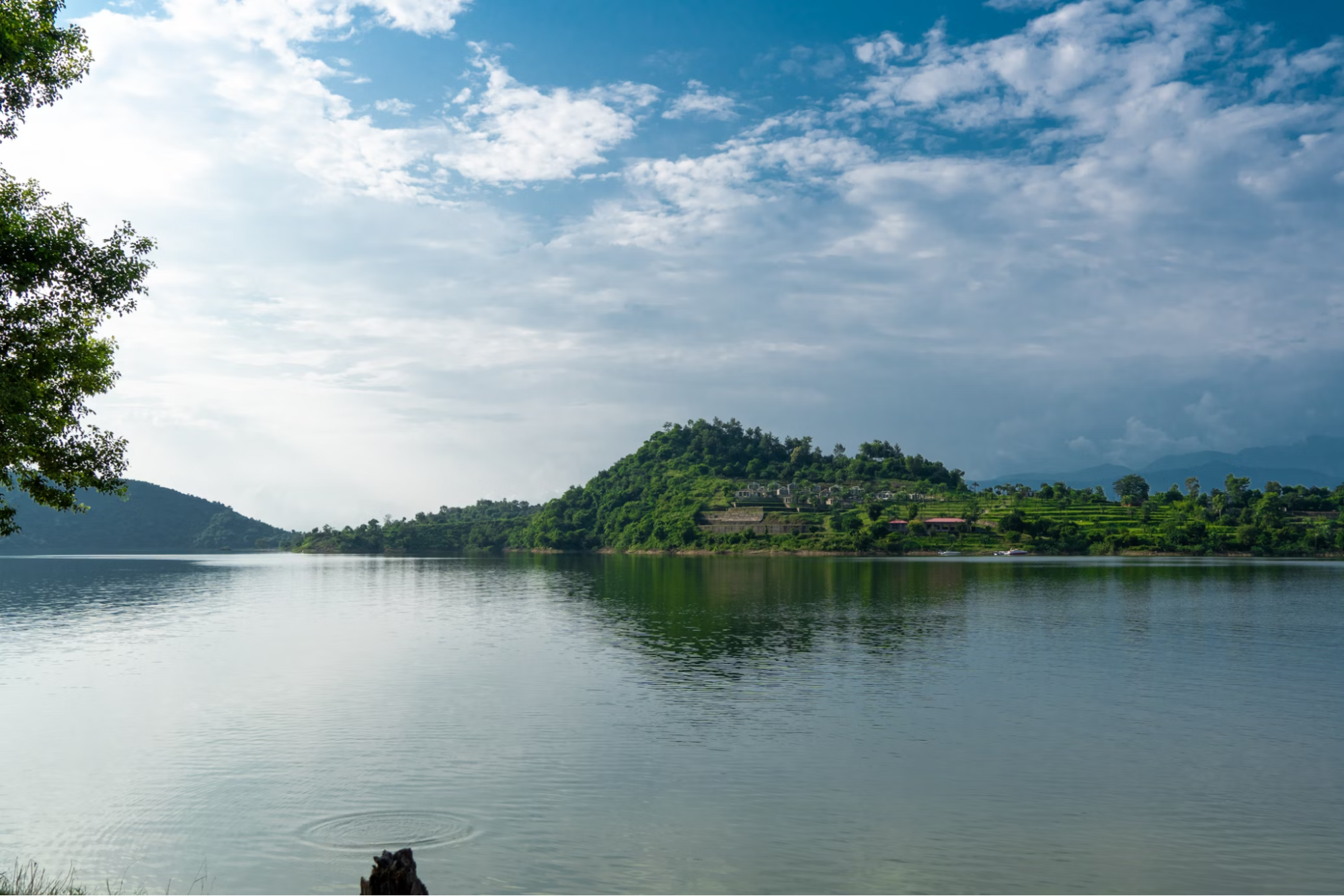 Scenic view of Bau Tro Lake surrounded by green hills under a cloudy sky