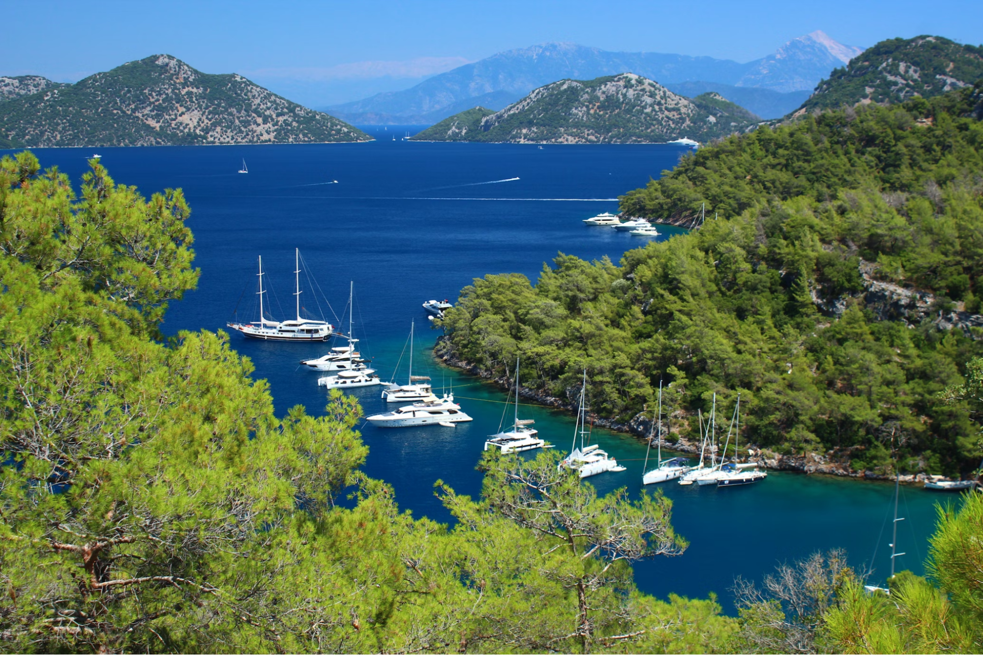 Boats anchored in a bay near Dalaman, Türkiye, with forested hills and clear blue water