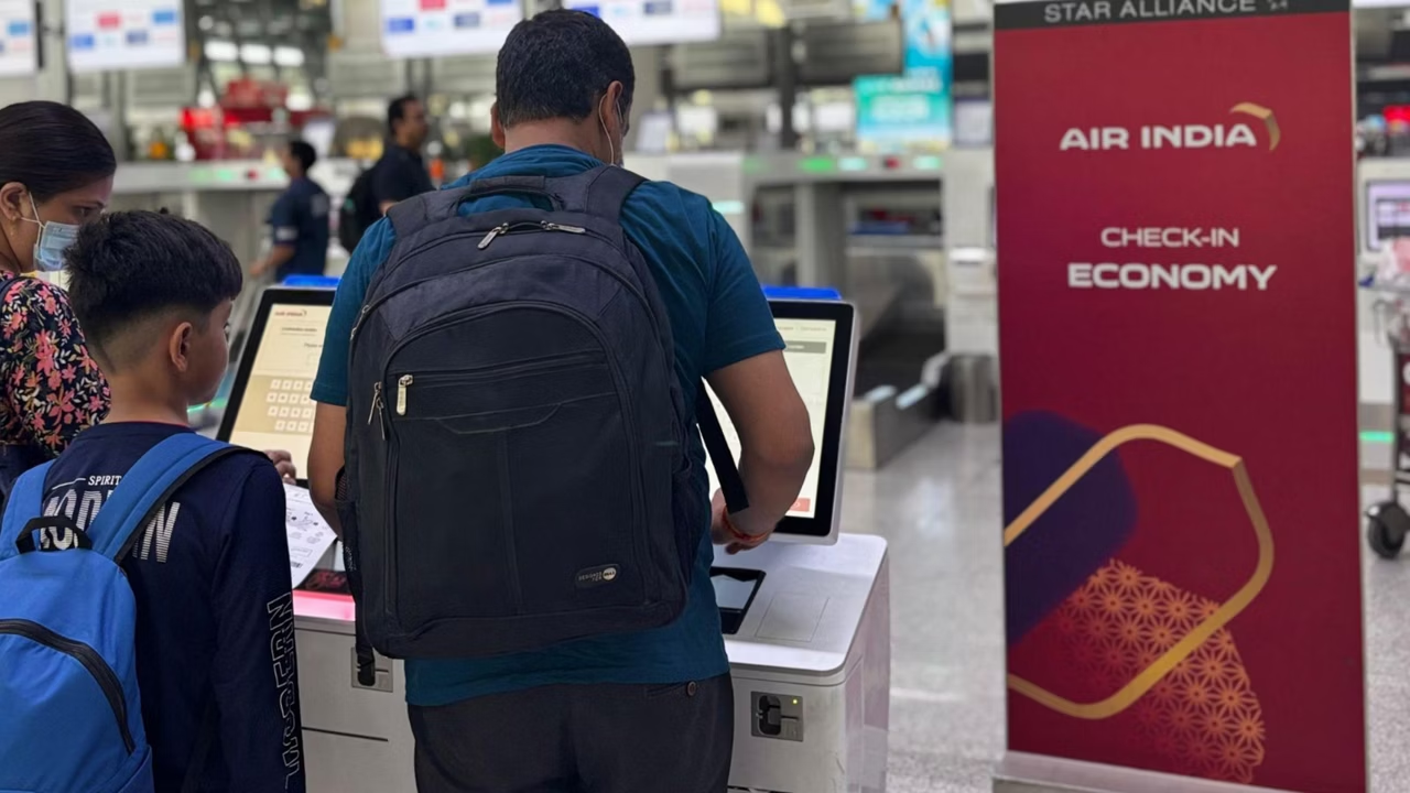 Passenger using Air India self-service check-in kiosk at the airport next to an Economy Class sign