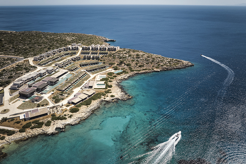 Aerial view of JW Marriott Crete Resort & Spa nestled along a rocky coastline with turquoise waters and boats nearby