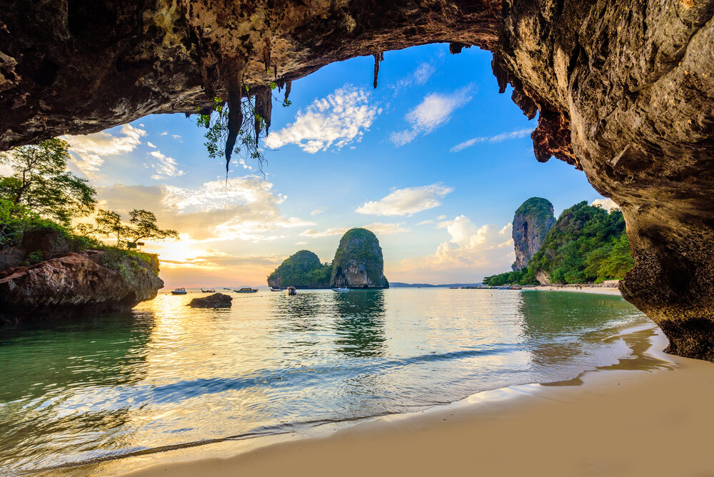View of limestone cliffs and calm sea from inside a coastal cave at sunset in Krabi